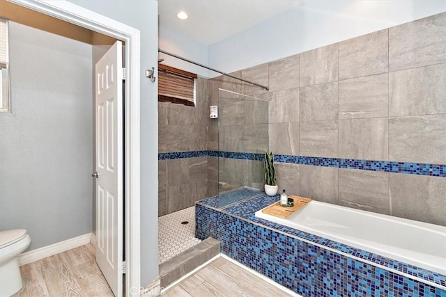 bathroom with toilet, wood finished floors, tiled tub, tiled shower, and baseboards