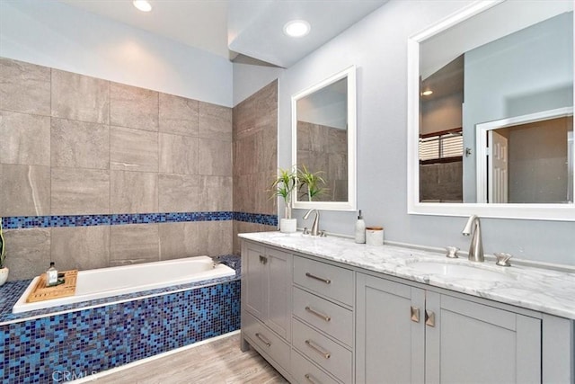 full bathroom with double vanity, a garden tub, a sink, and wood finished floors