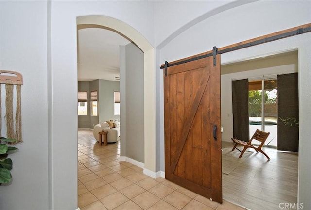 hall with arched walkways, light tile patterned floors, baseboards, and a barn door