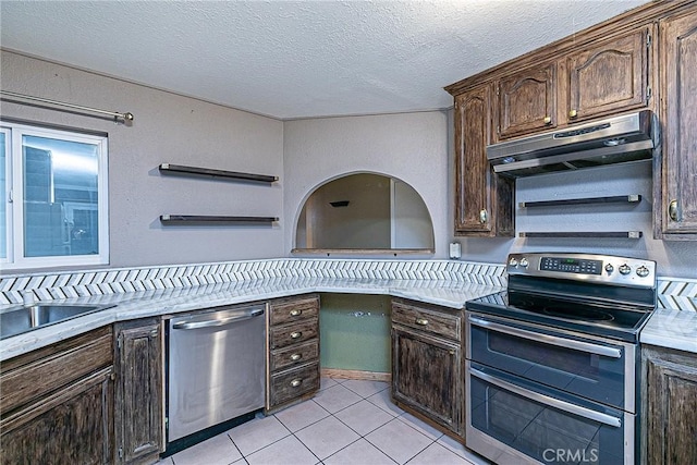 kitchen with light tile patterned floors, stainless steel appliances, dark brown cabinets, light countertops, and under cabinet range hood