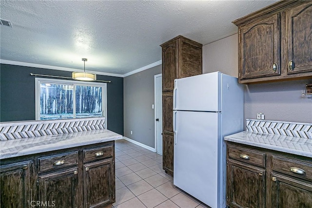 kitchen with light tile patterned floors, dark brown cabinets, ornamental molding, light countertops, and freestanding refrigerator