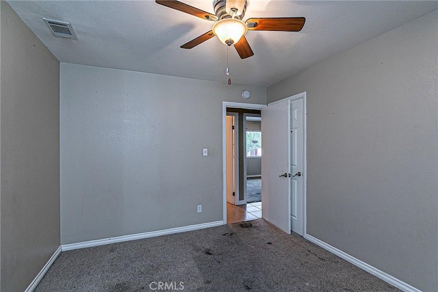 carpeted empty room with ceiling fan, visible vents, and baseboards