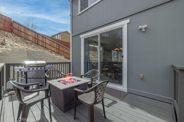 deck with an outdoor fire pit, grilling area, and fence