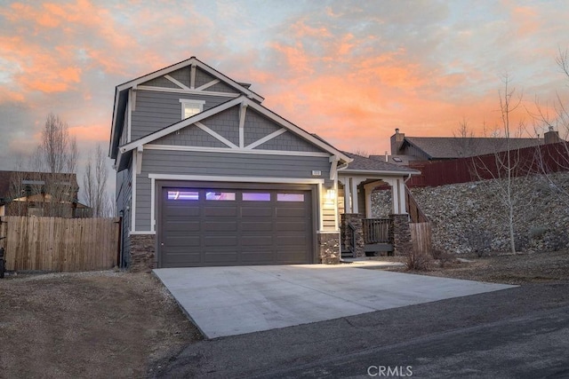 craftsman house with a garage, stone siding, driveway, and fence