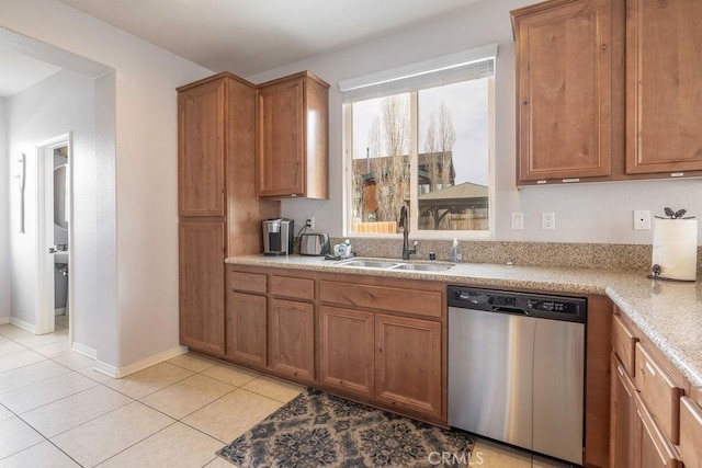 kitchen with light tile patterned floors, stainless steel dishwasher, brown cabinetry, a sink, and baseboards