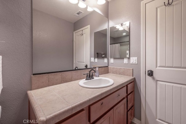 bathroom featuring visible vents, a textured wall, and vanity