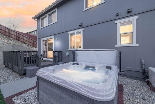 back of property at dusk featuring fence, a wooden deck, and a hot tub