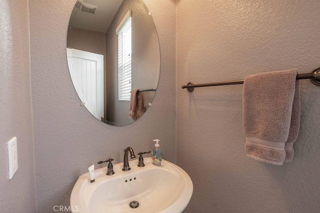 bathroom featuring a textured wall, visible vents, and a sink