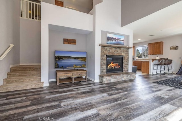 living room with baseboards, a towering ceiling, wood finished floors, stairs, and a stone fireplace