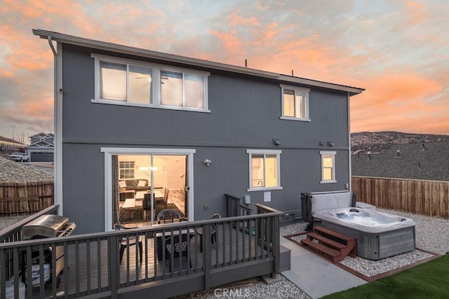 rear view of property with fence, a wooden deck, and a hot tub