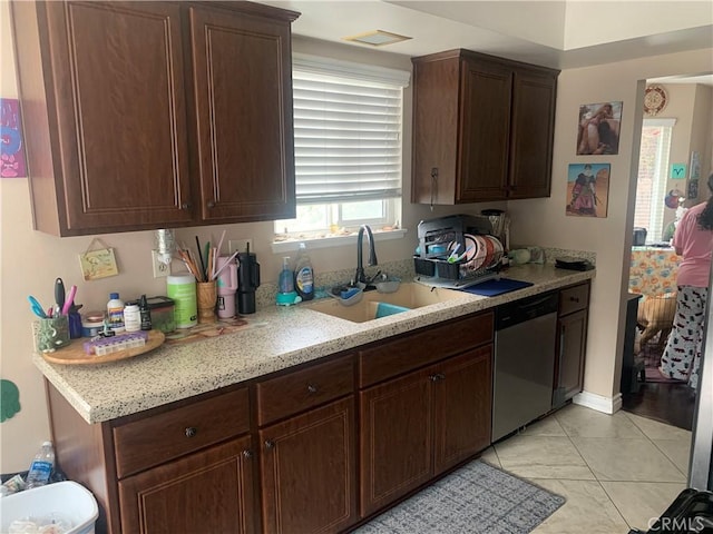 kitchen with light tile patterned floors, dark brown cabinetry, dishwasher, light stone countertops, and a sink