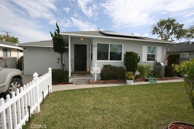 view of front of property with a front yard, solar panels, fence, and stucco siding