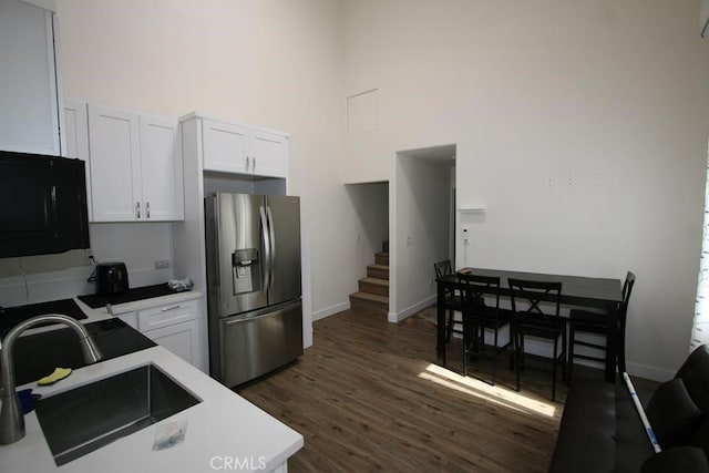 kitchen featuring stainless steel refrigerator with ice dispenser, a high ceiling, white cabinetry, a sink, and black microwave