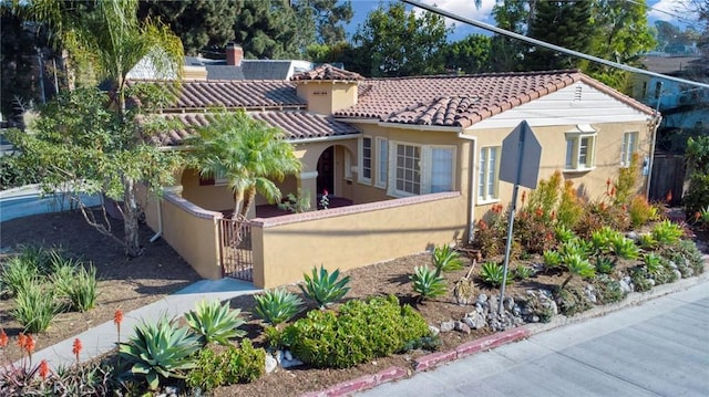 mediterranean / spanish home with a fenced front yard, a tile roof, a gate, and stucco siding