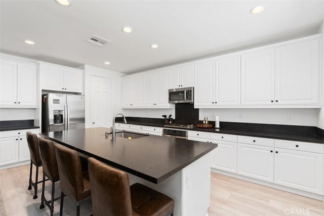 kitchen with stainless steel appliances, a sink, visible vents, a kitchen breakfast bar, and dark countertops