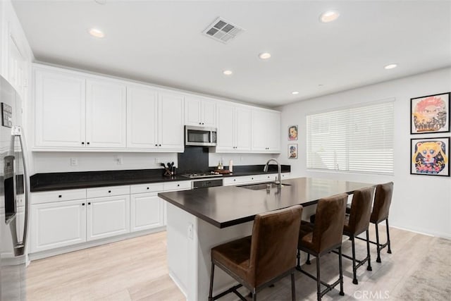 32345 Jeter Ln, Menifee, CA 92584 - kitchen featuring stainless steel appliances, a breakfast bar area, dark countertops, light wood-style flooring, and white cabinets