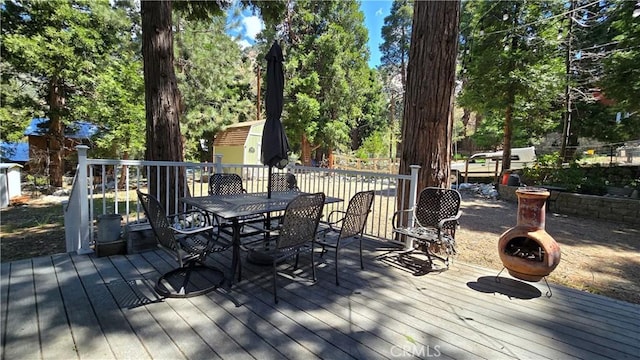 wooden terrace featuring an outbuilding, outdoor dining area, and a storage unit