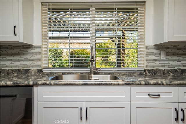 kitchen with dark countertops, white cabinets, decorative backsplash, and a sink