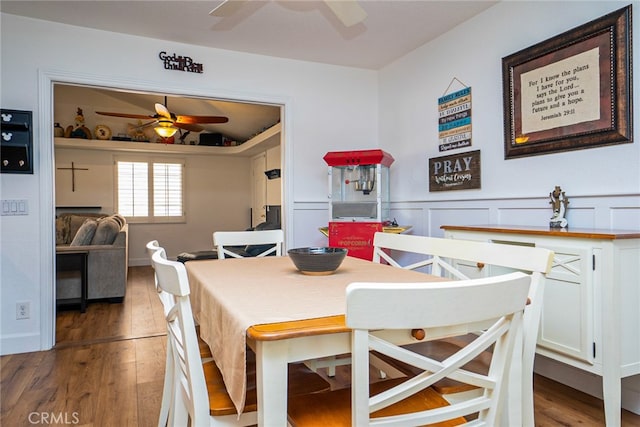 dining space featuring ceiling fan, vaulted ceiling, a wainscoted wall, and wood finished floors