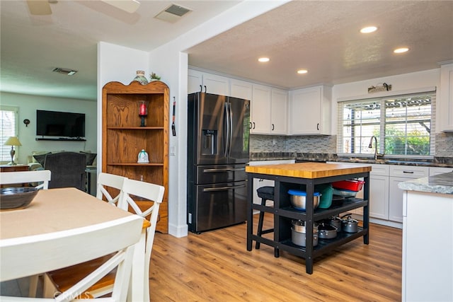 kitchen featuring a sink, visible vents, white cabinets, stainless steel fridge with ice dispenser, and light wood finished floors