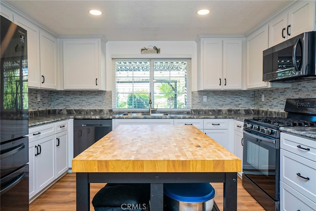 kitchen with black appliances, light wood finished floors, a sink, and white cabinets