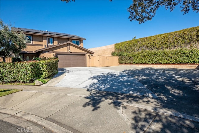 view of front of house featuring concrete driveway, stucco siding, a gate, and roof mounted solar panels