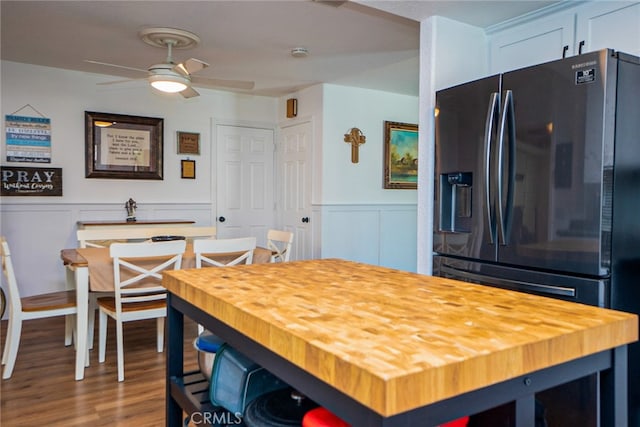 interior space featuring butcher block countertops, wainscoting, black refrigerator with ice dispenser, and ceiling fan