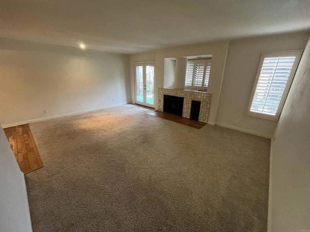 unfurnished living room with carpet floors, baseboards, french doors, and a tile fireplace