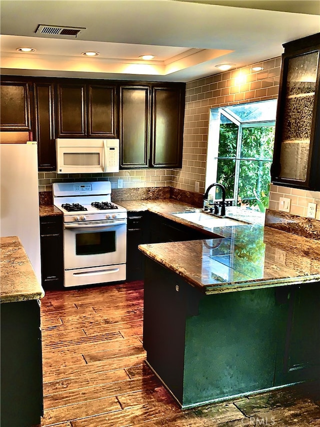 kitchen featuring a peninsula, white appliances, dark wood-type flooring, a sink, and tasteful backsplash