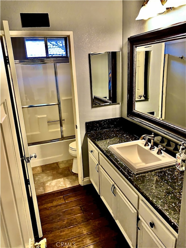 full bathroom featuring enclosed tub / shower combo, a textured wall, toilet, wood finished floors, and vanity