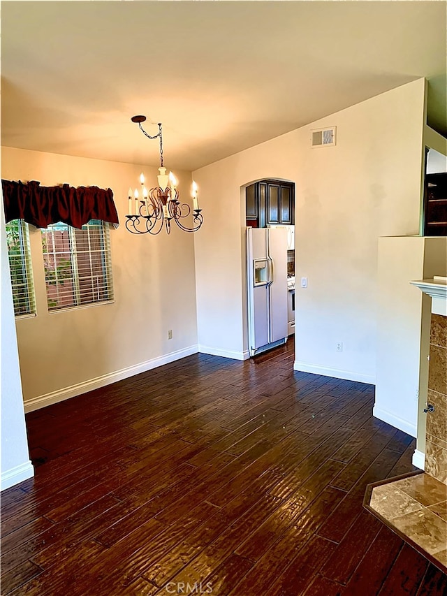 spare room with baseboards, visible vents, a tiled fireplace, dark wood-style flooring, and a chandelier