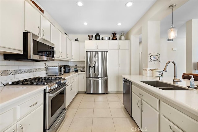 kitchen with stainless steel appliances, a sink, white cabinets, light countertops, and backsplash