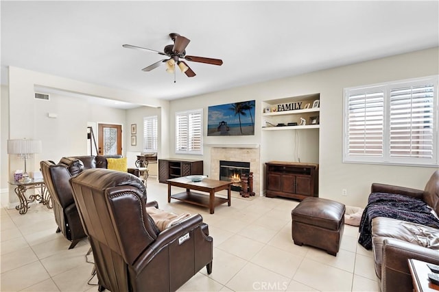 living area featuring built in shelves, light tile patterned floors, visible vents, a glass covered fireplace, and ceiling fan