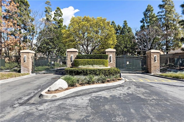 community / neighborhood sign featuring fence and a gate