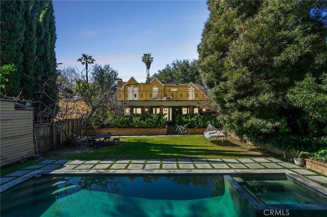 back of house featuring a yard, a balcony, an in ground hot tub, a fenced backyard, and an outdoor pool