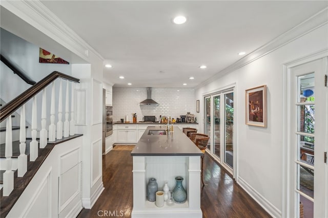 kitchen with dark wood-type flooring, a sink, ornamental molding, wall chimney range hood, and dark countertops