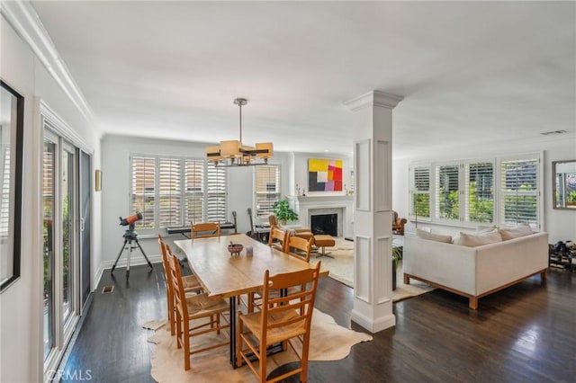 dining room with a fireplace, a notable chandelier, decorative columns, ornamental molding, and wood finished floors