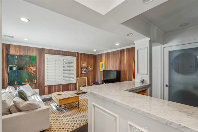 kitchen featuring light stone counters, visible vents, ornamental molding, and wooden walls