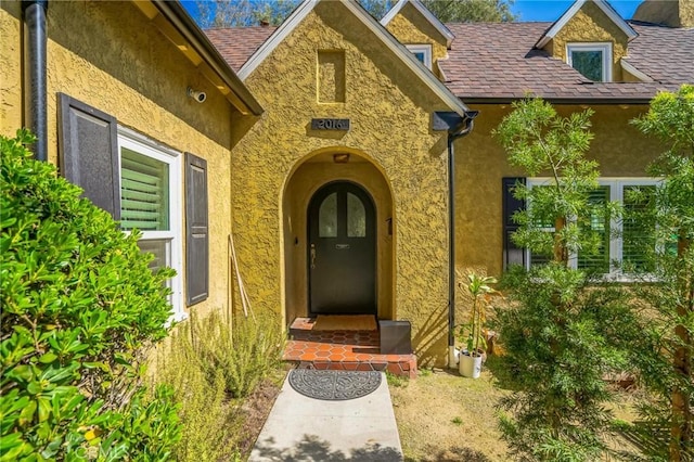 property entrance featuring roof with shingles and stucco siding