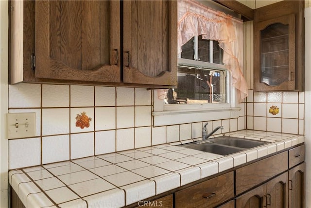 kitchen with tile countertops, backsplash, and a sink