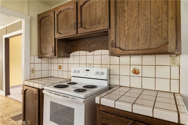 kitchen featuring tasteful backsplash, electric range, crown molding, and tile countertops