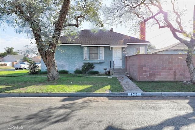 view of front of property featuring a front lawn, a shingled roof, fence, and stucco siding