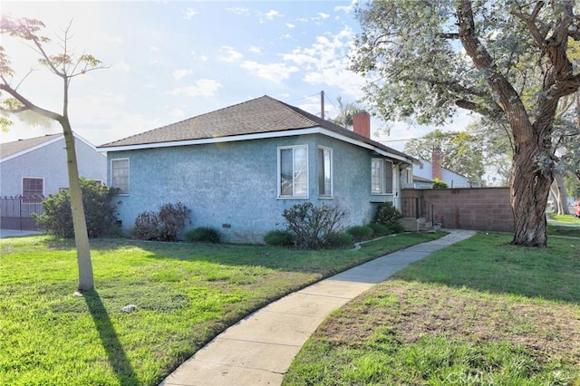 view of property exterior with a yard, a chimney, stucco siding, a shingled roof, and fence