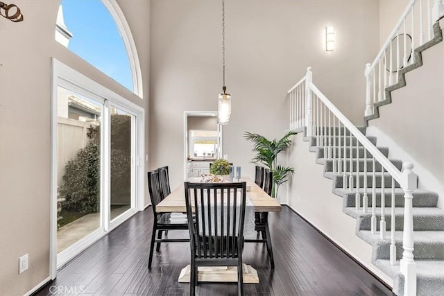 dining room featuring dark wood-style floors, baseboards, stairway, and a high ceiling