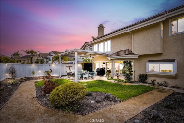 back of property with a patio, a fenced backyard, a lawn, stucco siding, and a chimney