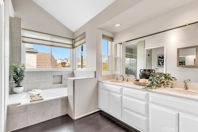 bathroom featuring vaulted ceiling, a sink, a bath, and double vanity