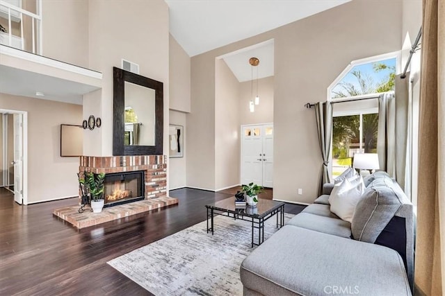 living area featuring a brick fireplace, visible vents, high vaulted ceiling, and wood finished floors