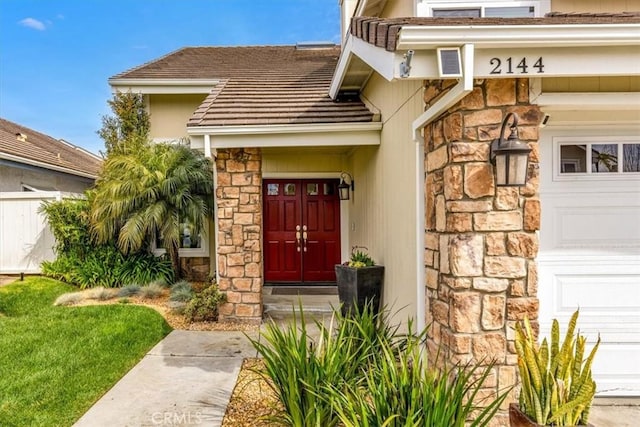 property entrance featuring an attached garage, stone siding, visible vents, and fence