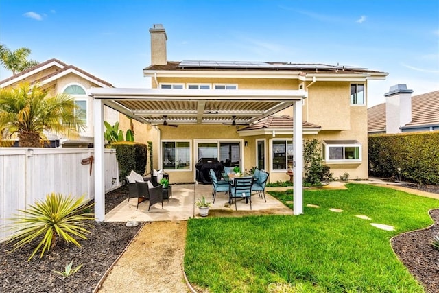 back of property featuring a patio, fence, a yard, roof mounted solar panels, and stucco siding