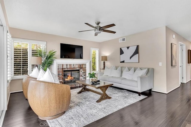 living room featuring dark wood-style floors, visible vents, a brick fireplace, ceiling fan, and baseboards